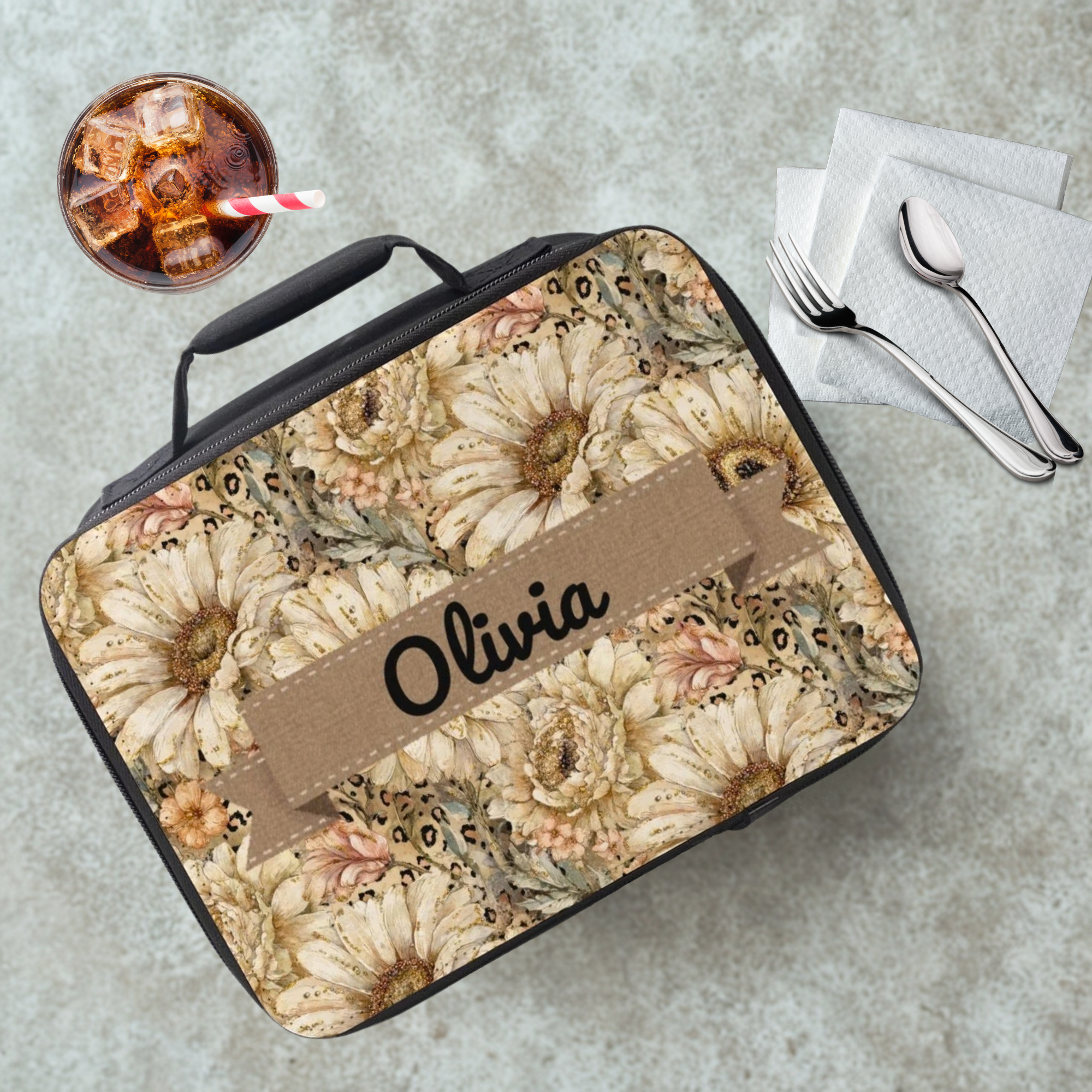 Floral patterned lunch bag with 'Olivia' custom text on a cafeteria table with a drink and utensils.