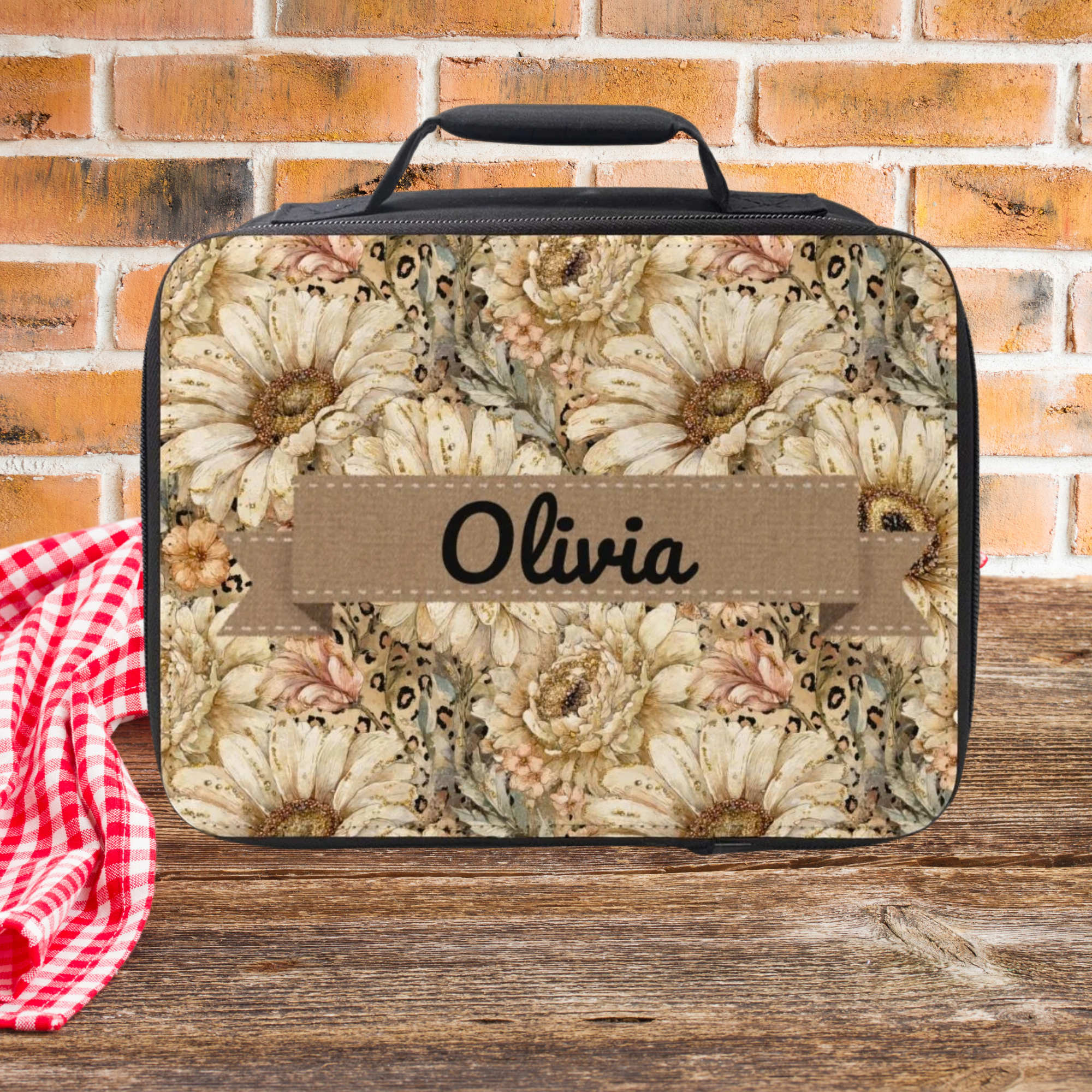 Floral patterned lunch bag with 'Olivia' personalized text on a wooden picnic table against a brick wall background