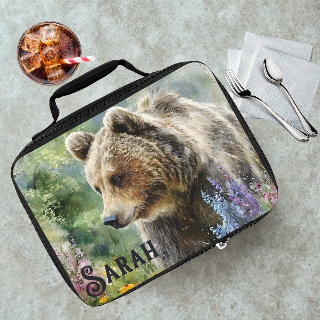 Lunch bag with bear design and 'Sarah' personalized text on a cafeteria table with a drink and utensils.