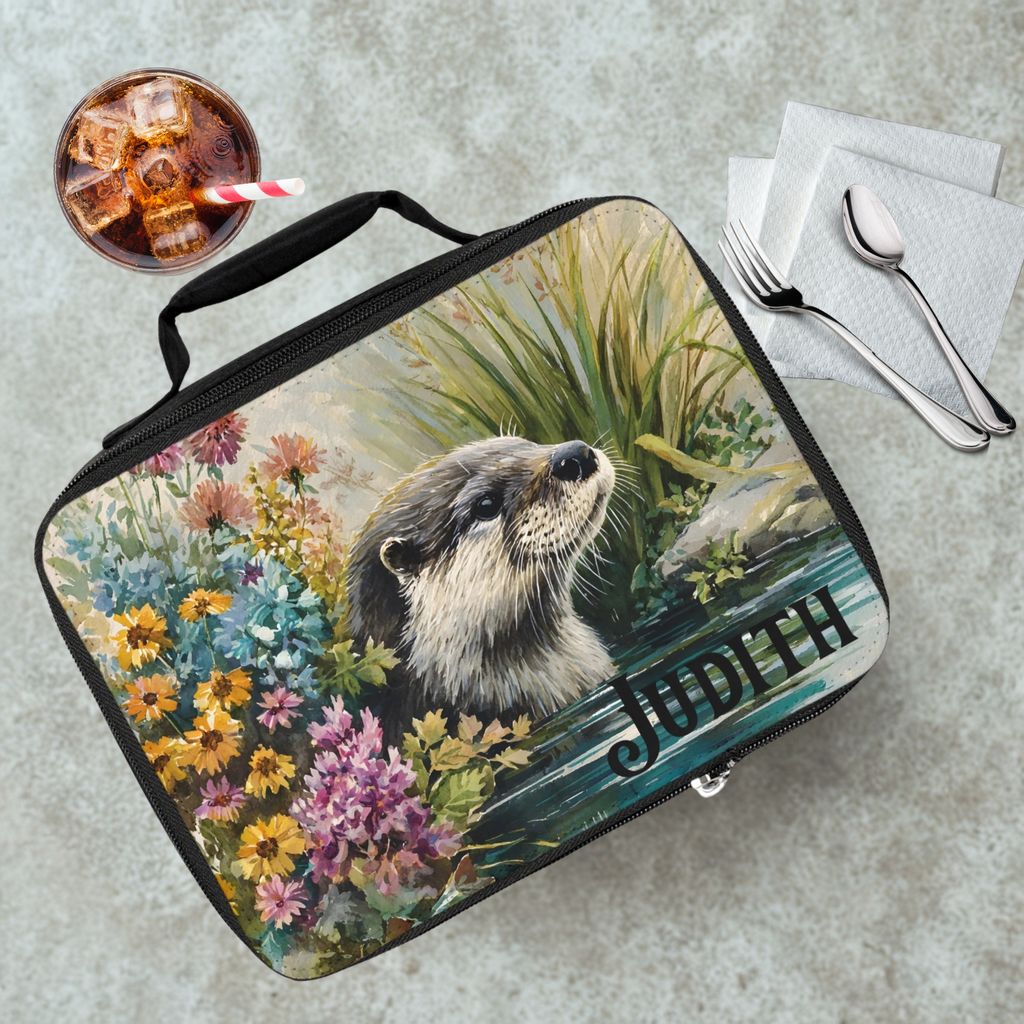 Lunch bag with an otter design and 'Judith' text on a table with a drink and utensils.