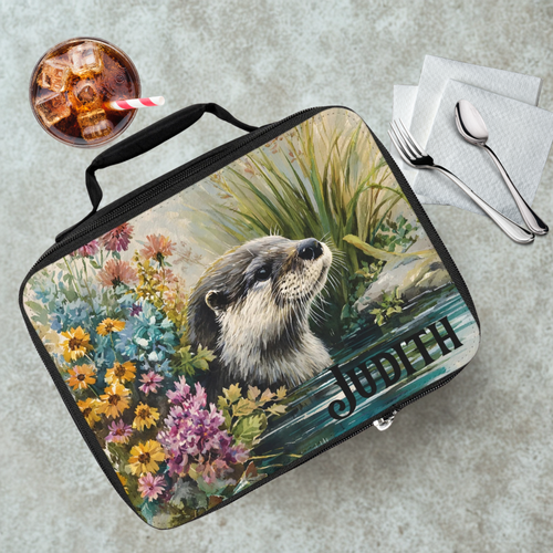 Lunch bag with an otter design and 'Judith' text on a table with a drink and utensils.