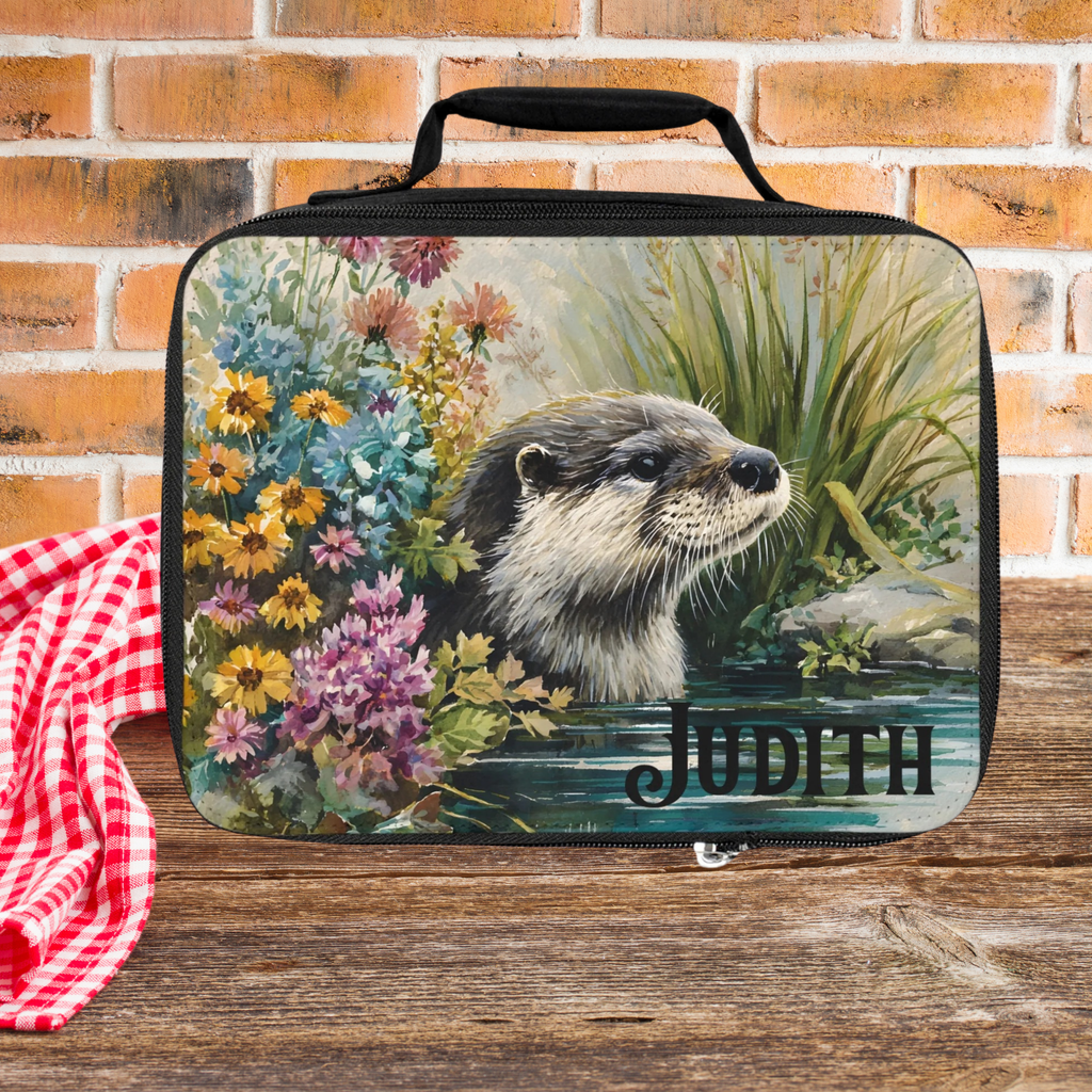 Lunch bag with an otter design and 'Judith' personalized text, placed on a wooden picnic table with a brick wall background.