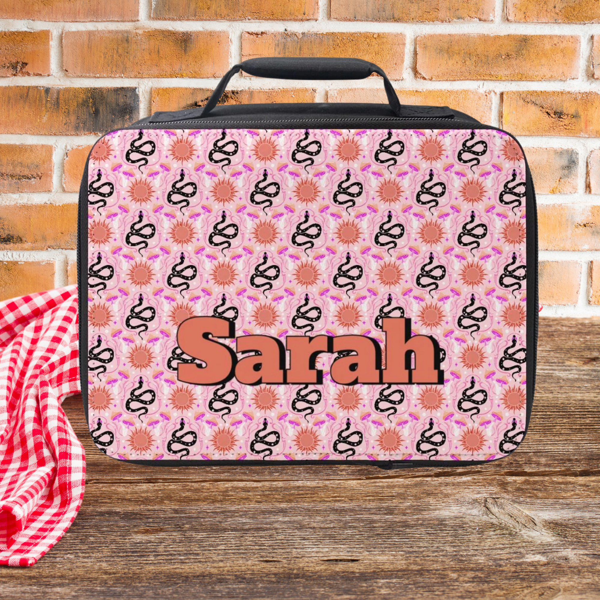 Pink patterned lunch bag with 'Sarah' on it against a brick wall background