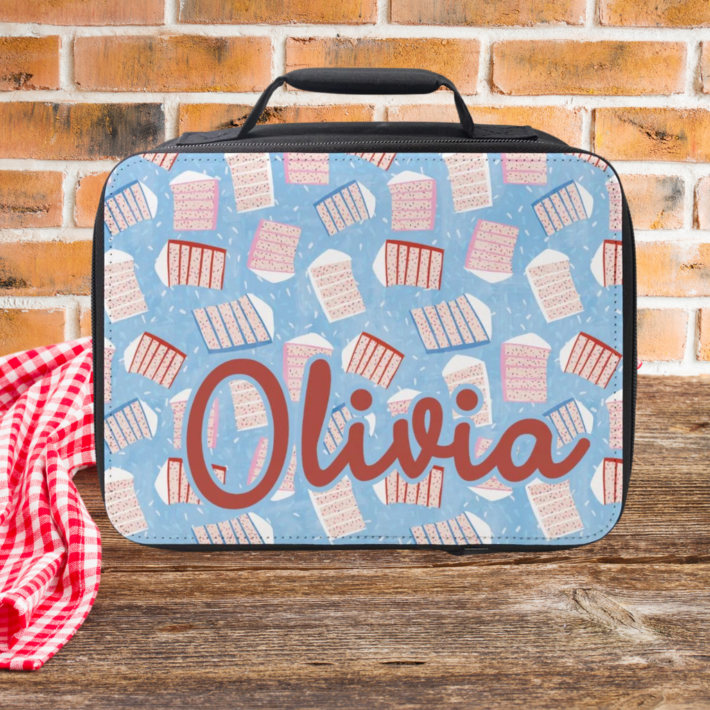  insulated lunch bag with a sliced cake pattern and 'Olivia' custom text on a wooden picnic table and brick wall background