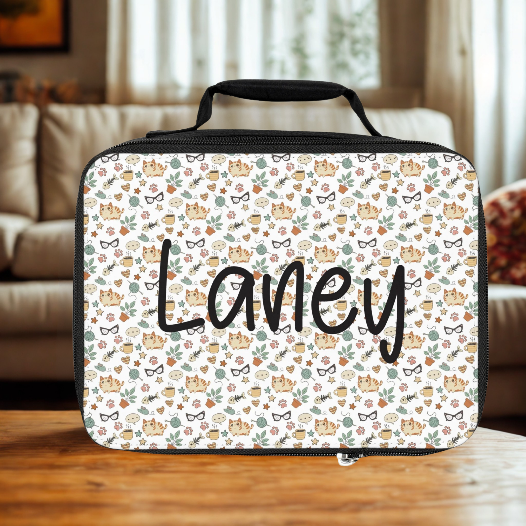  insulated lunch bag with 'Laney' custom text and a cat pattern on a wooden living room table.