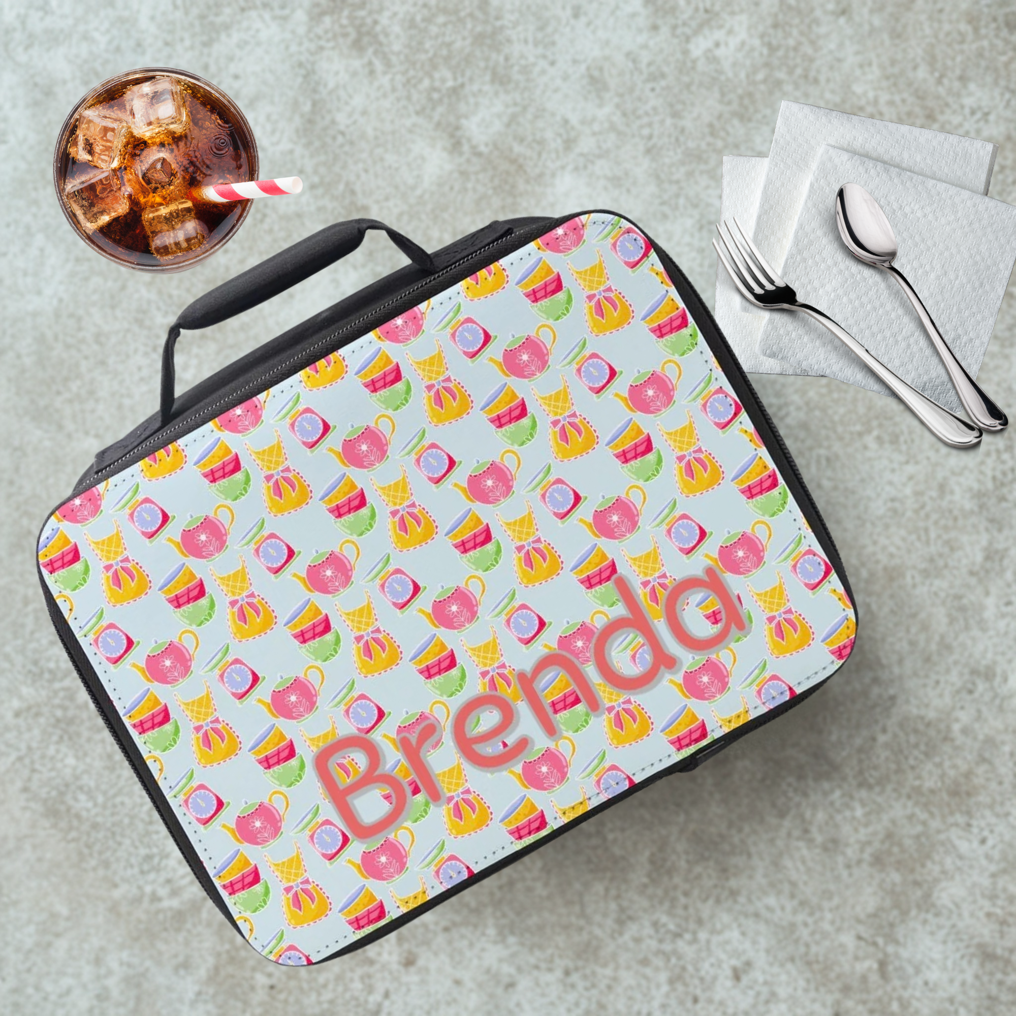 Colorful patterned lunch bag with 'Brenda' on a gray table with a drink and utensils.