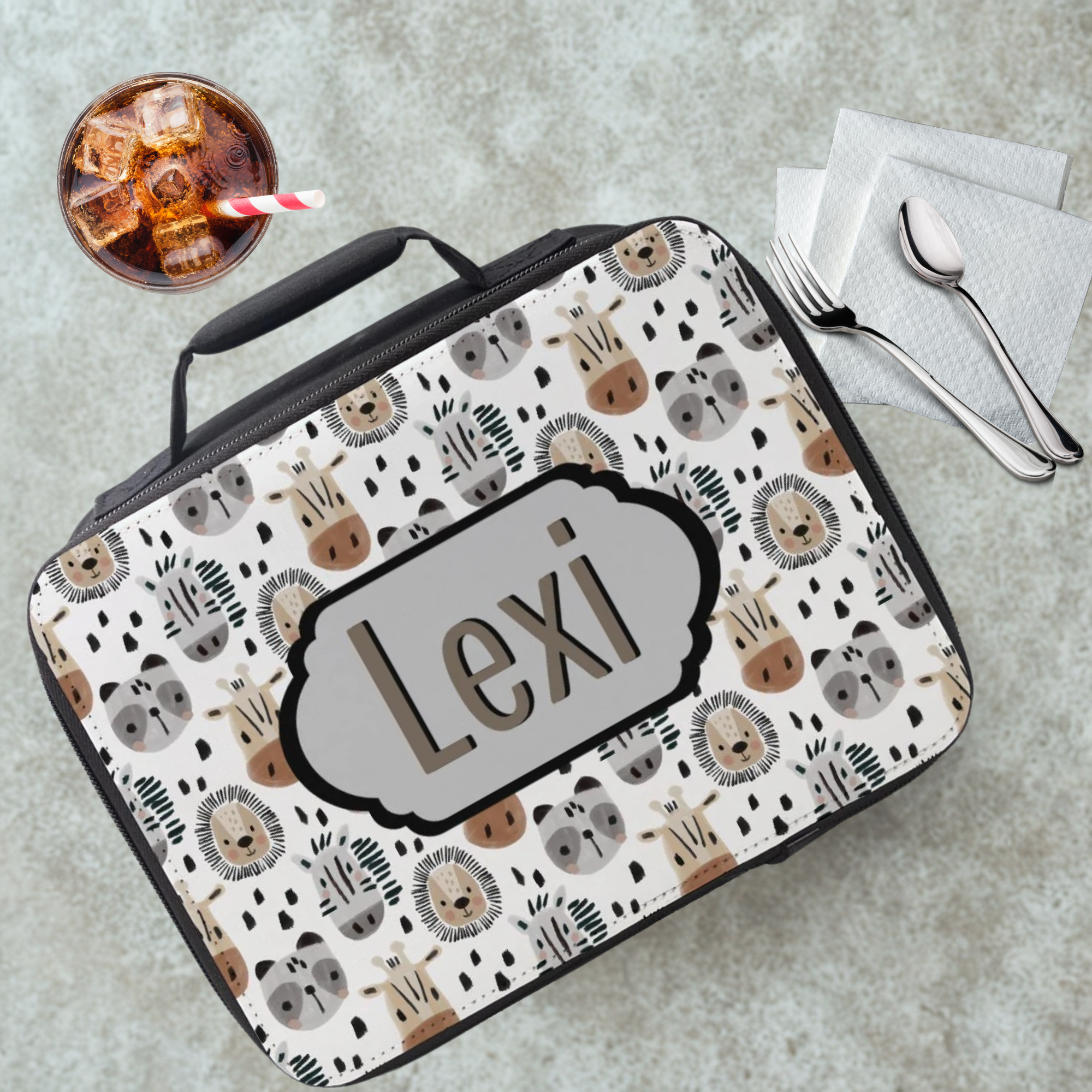 Lunch bag with animal pattern and 'Lexi' name on a table with a drink and utensils.
