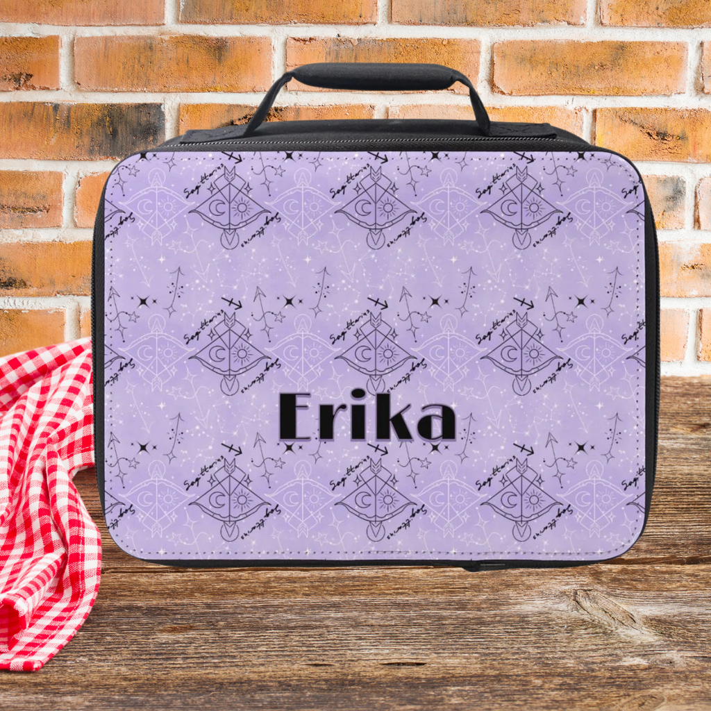 Lunch bag with purple and black Sagittarius zodiac pattern and 'Erika' custom text on a wooden picnic table against a brick wall background