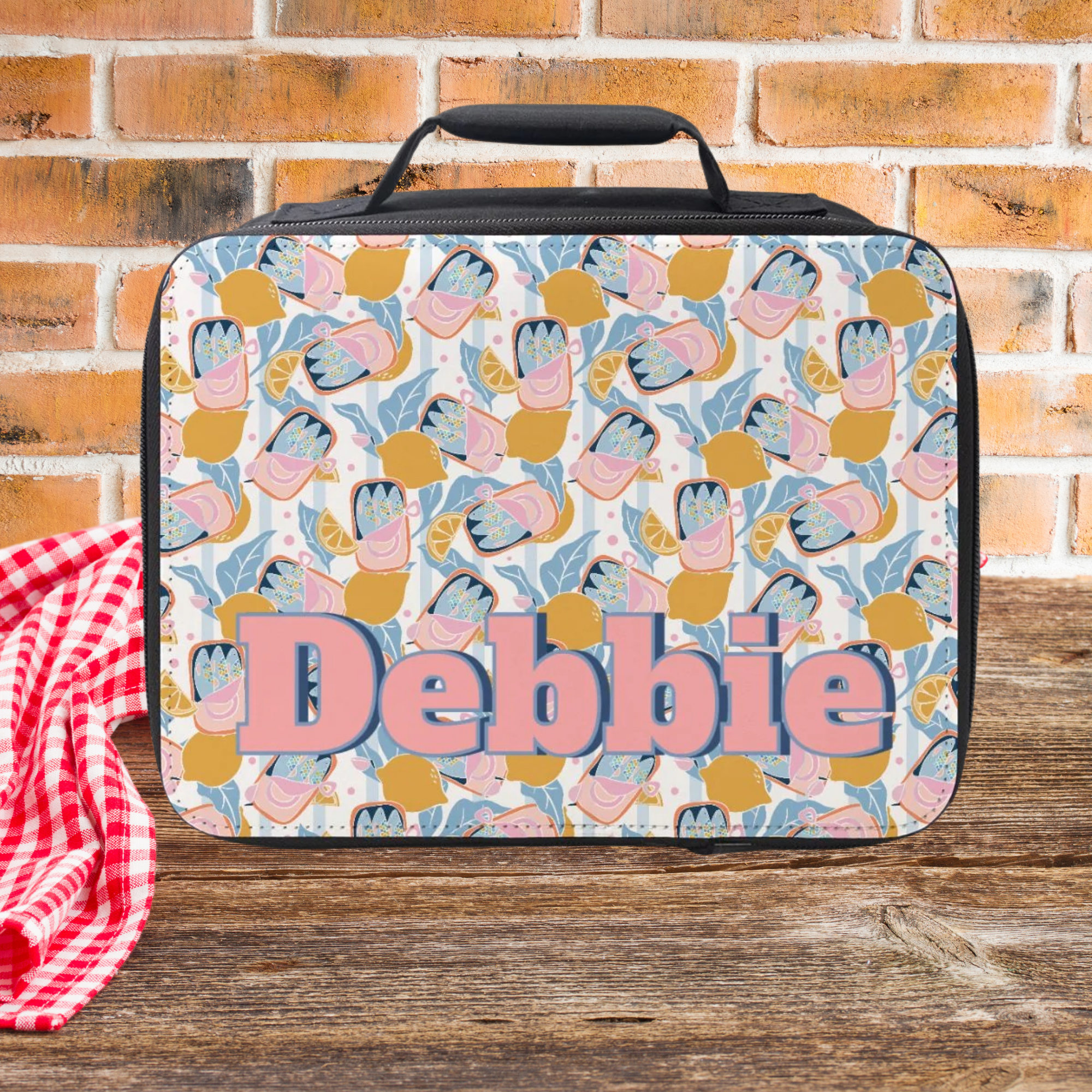  insulated lunch bag with colorful sardine lemon pattern and 'Debbie' personalized text on a wooden picnic table with brick background