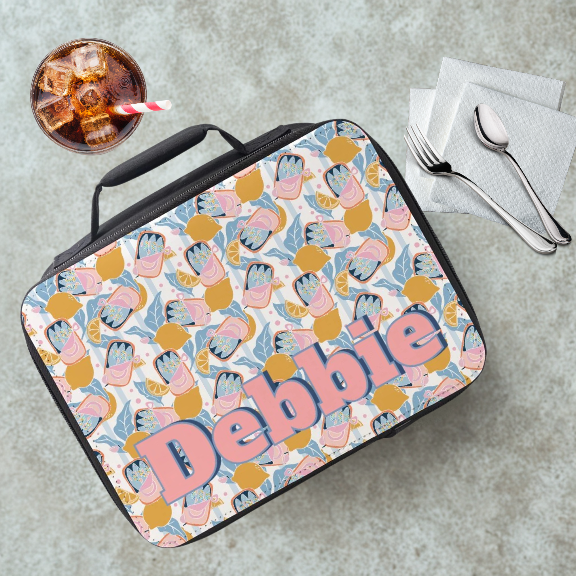 Lunch bag with colorful sardine lemon pattern and 'Debbie' custom text on a cafeteria table with a drink and utensils.