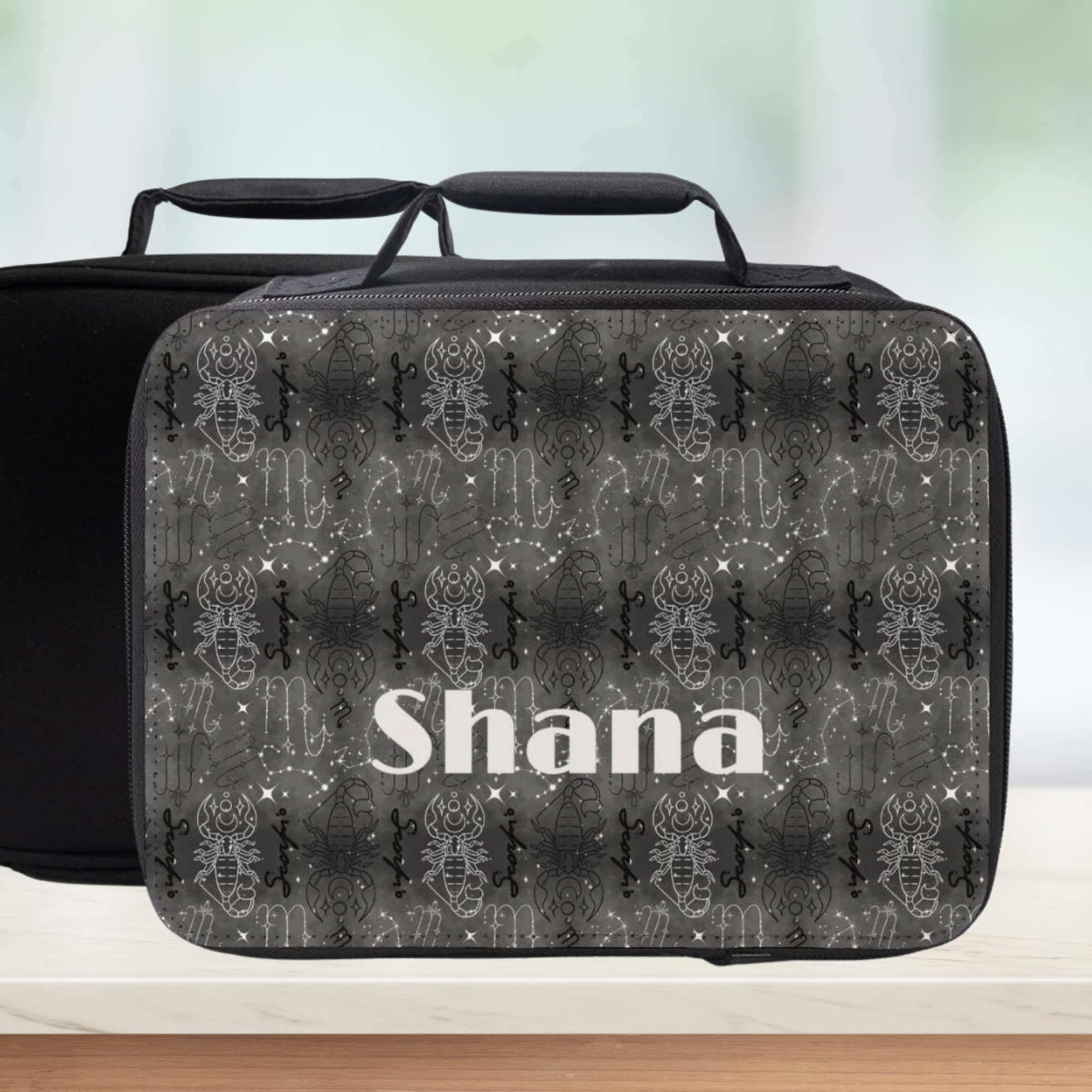 Black and gray Scorpio patterned lunch bag with 'Shana' personalization on a blurred background