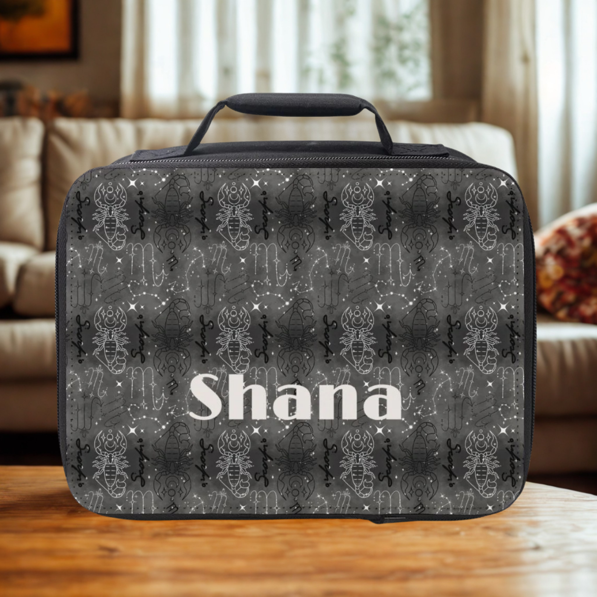 Black and white Scorpio patterned lunch bag with 'Shana' name printed on a wooden coffee table in a cozy living room.