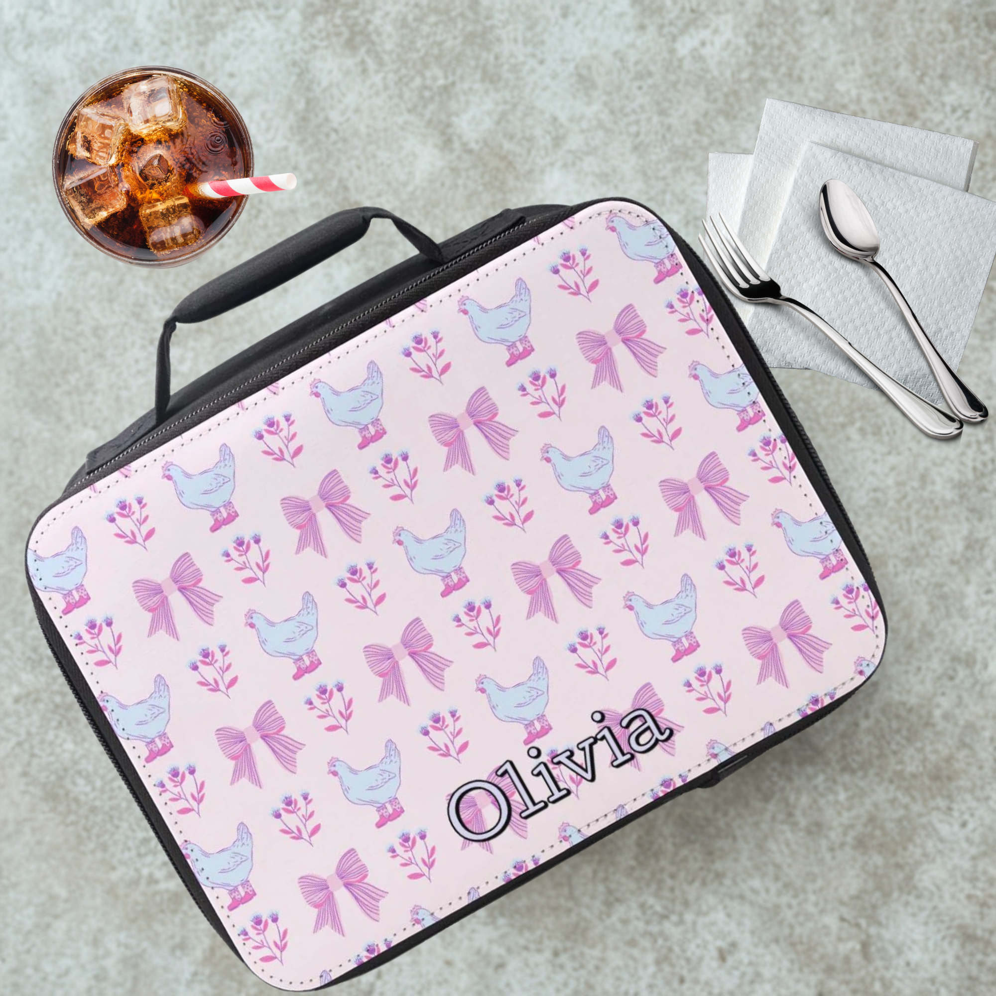 Personalized lunch bag with chicken and bow pattern on a gray table with a drink and utensils.