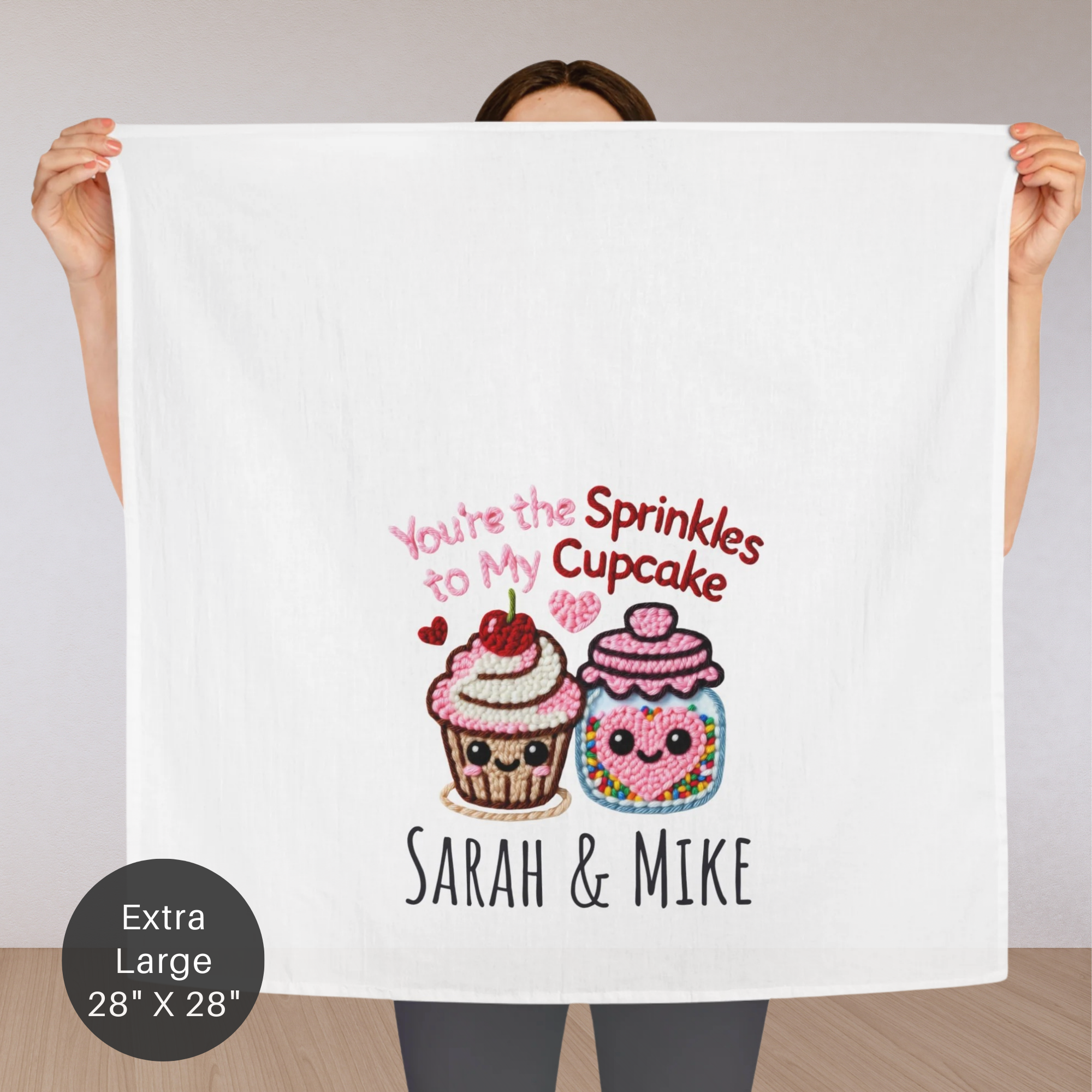 Person holding an extra large tea towel with cartoon cupcakes and text design.