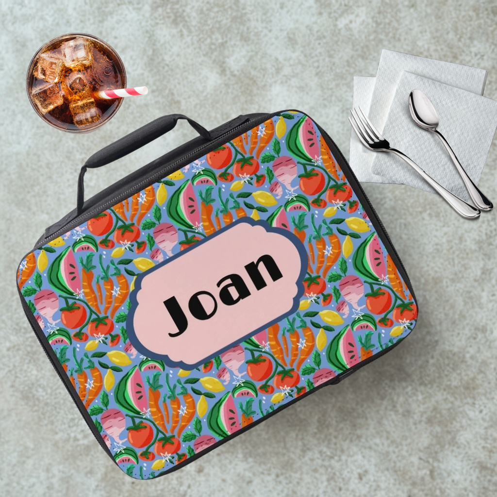 Colorful fruit patterned lunch bag with 'Joan' nameplate on a table with a drink and utensils.