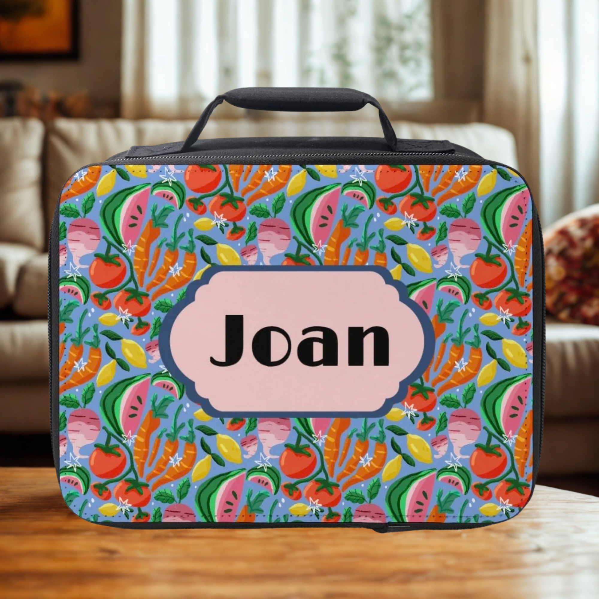 Colorful fruit-patterned lunch bag with 'Joan' on a wooden table in a cozy living room.