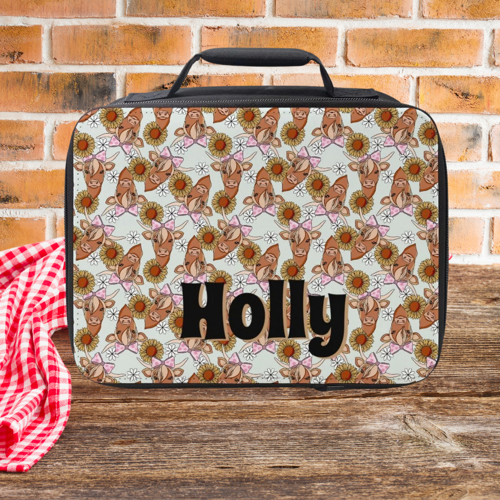 Lunch bag with floral pattern and 'Holly' text on a wooden picnic table with brick background