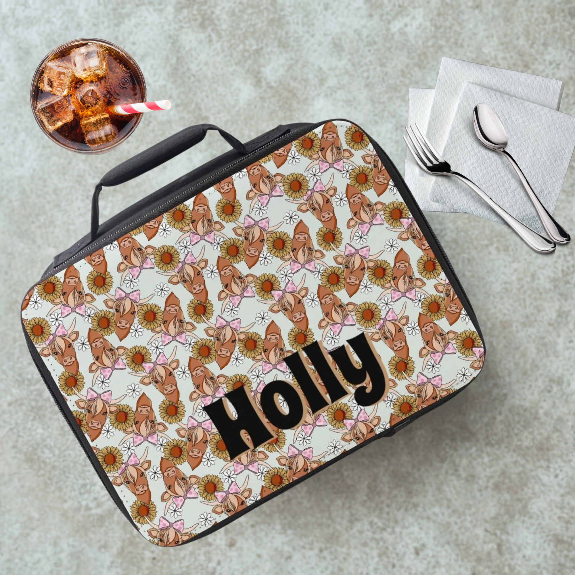 Lunch bag with highland cow  pattern on a cafeteria table with a drink and utensils.