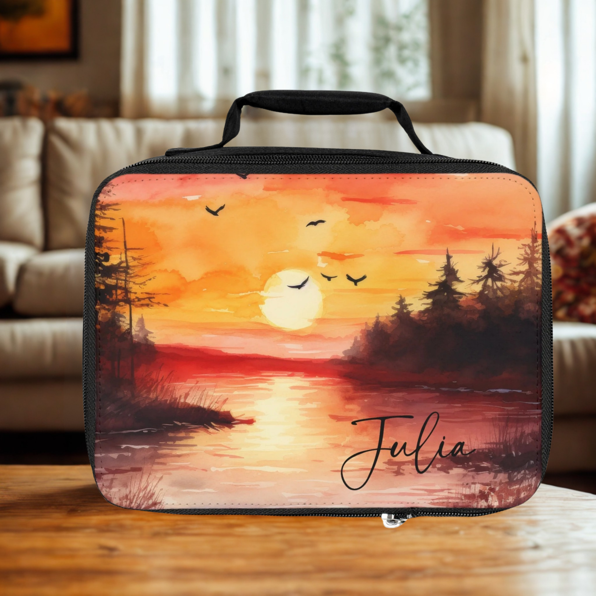  insulated lunch bag with sunset design and 'Julia' text on a wooden living room table.