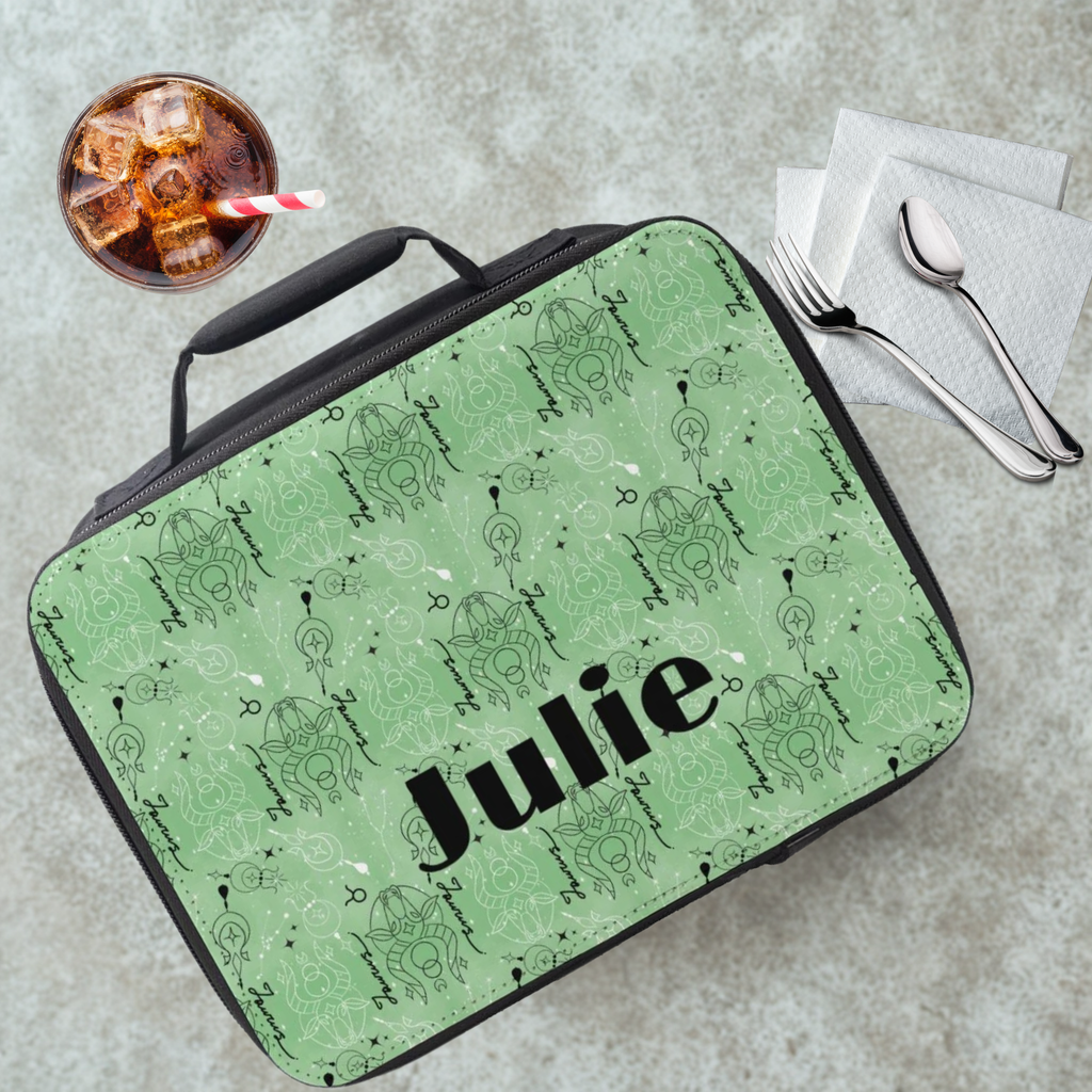Green Taurus zodiac pattern lunch bag with 'Julie' printed on it, placed on a cafeteria table with a drink and utensils in the background.