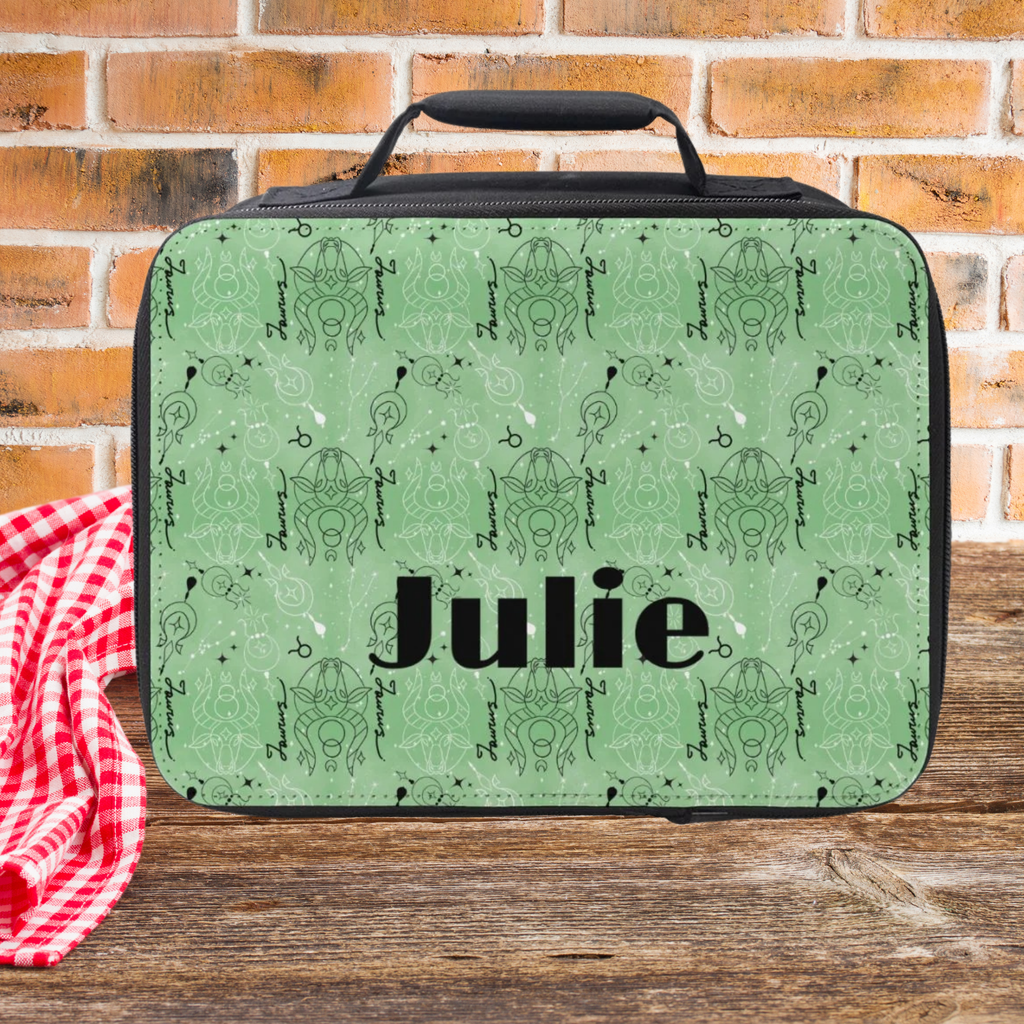  lunch bag with green and black Taurus zodiac symbols and 'Julie' printed on it, placed on a wooden surface with a brick wall background.
