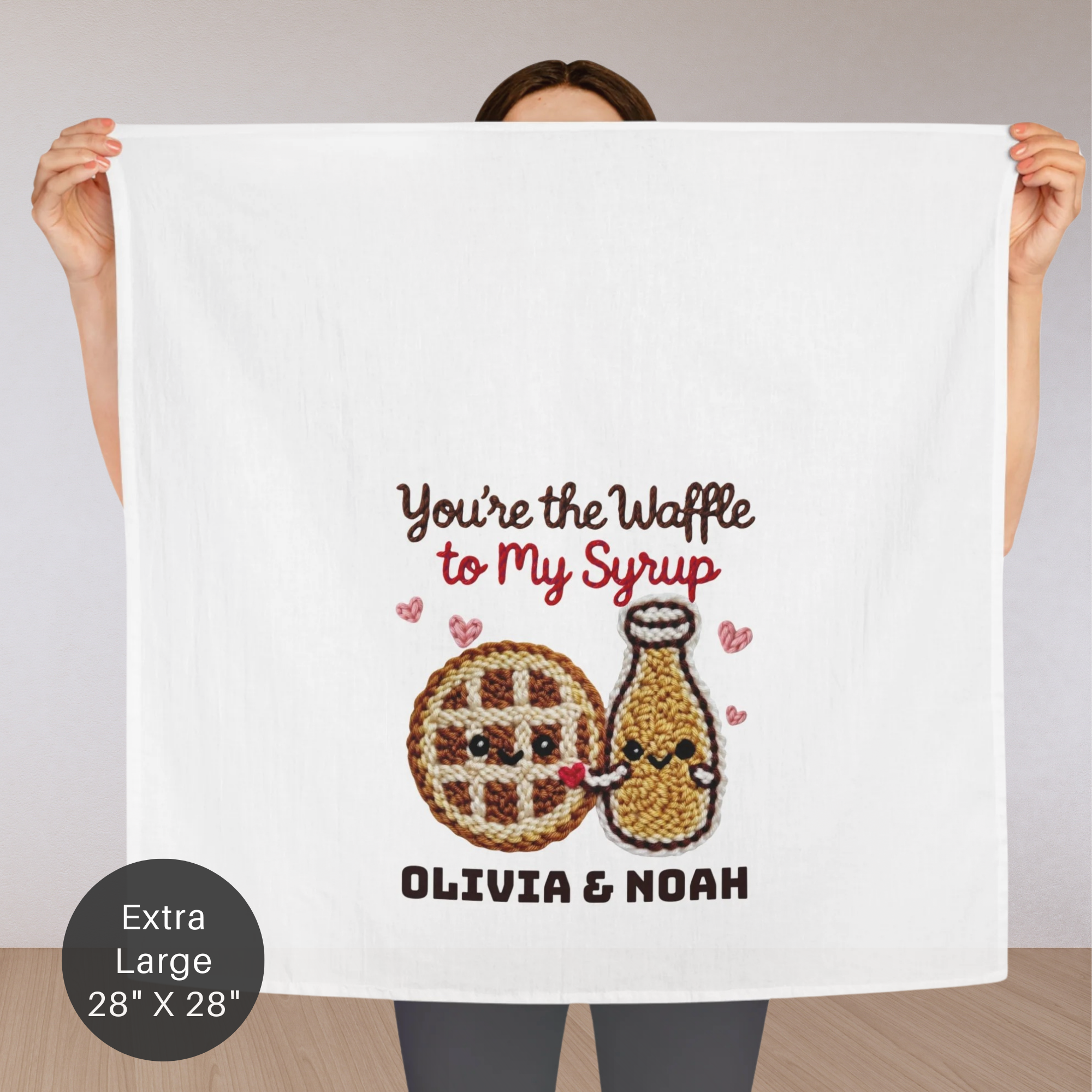 Person holding an extra large white tea towel with waffle and syrup design and text.