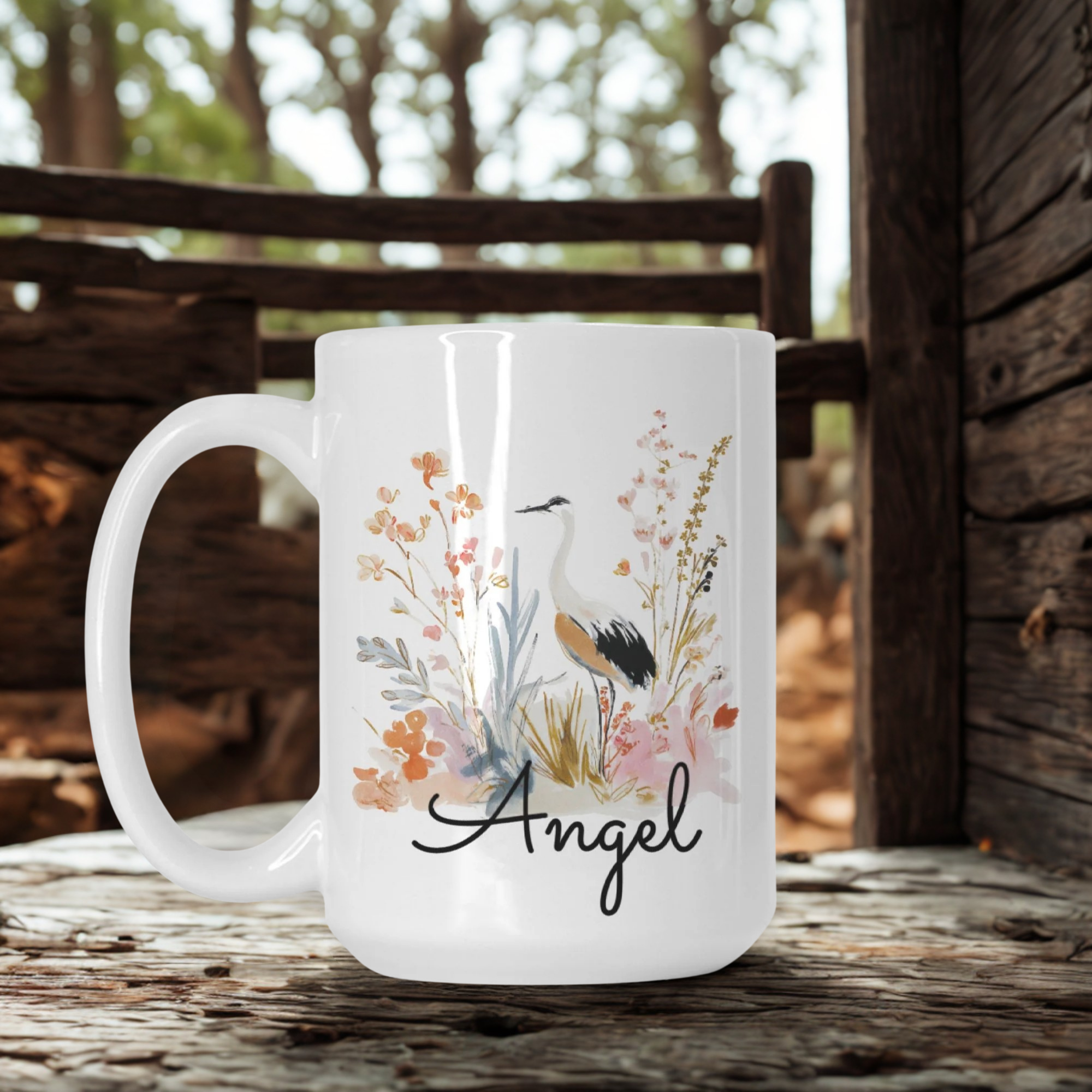 White mug with bird and floral design and 'Angel' text on a wooden surface.