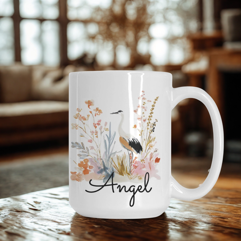 White mug with floral design and 'Angel' text on a wooden table in a cozy room.