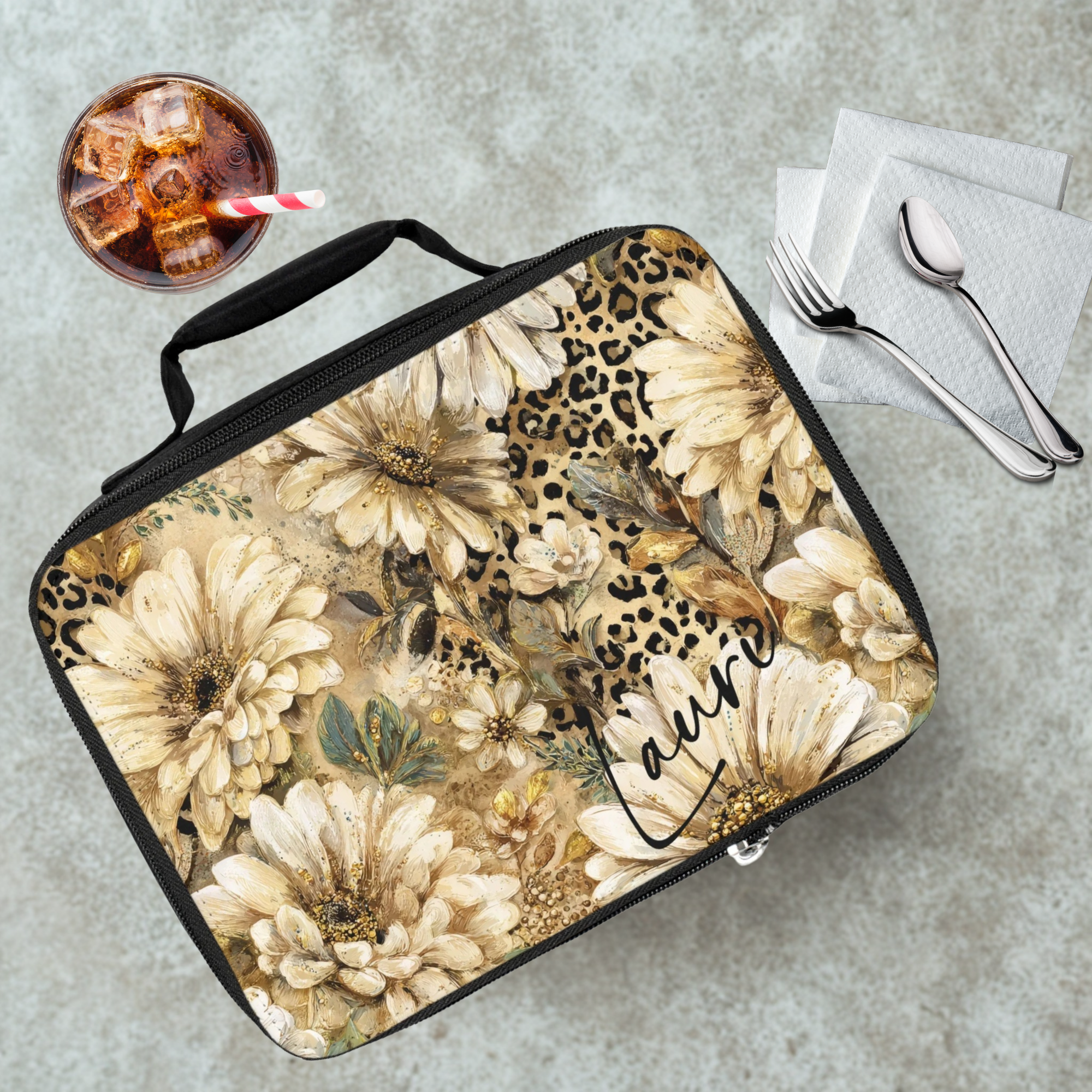 Floral and leopard print patterned lunch bag with personalized name on a cafeteria table with a drink and utensils.