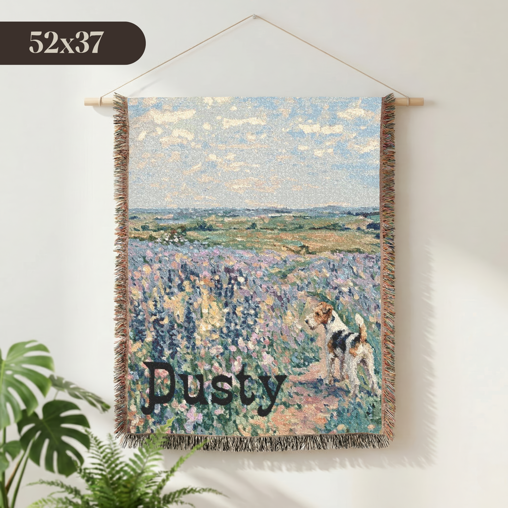 A woven wall tapestry featuring an impressionistic lavender field landscape with a dog and the name 'Dusty' in script, hanging on a light wall with a plant visible at the lower left.