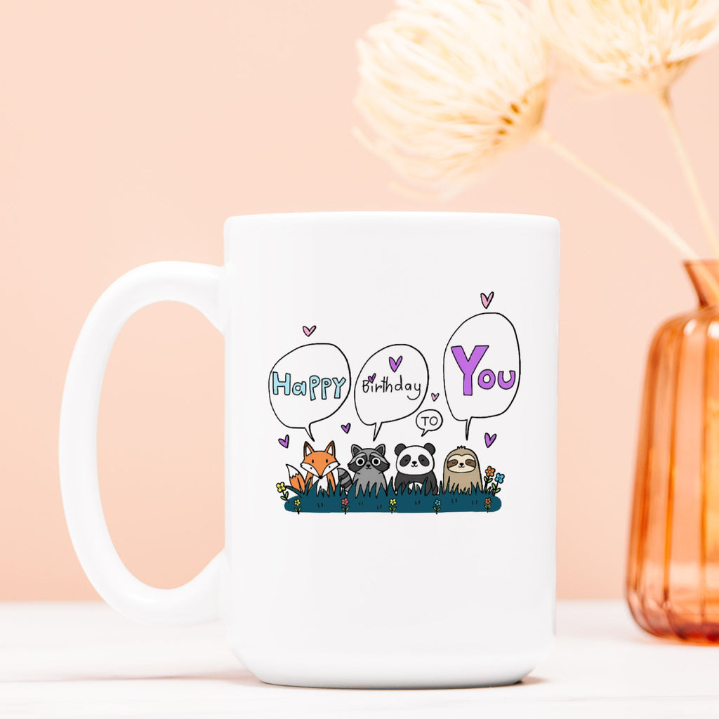 White mug with cartoon animals and 'Happy Birthday You' text on a light pink background