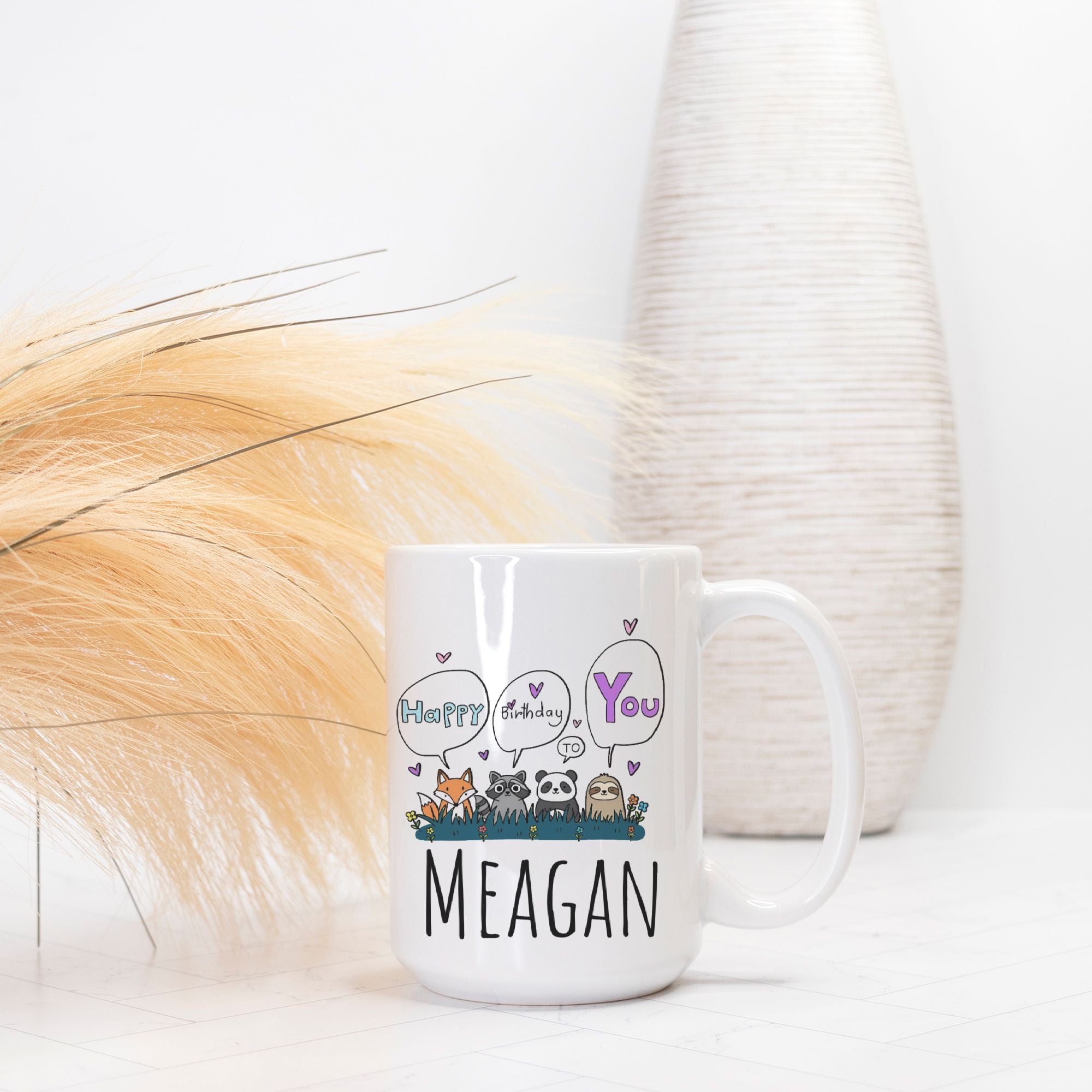 White mug with cartoon animals and text 'Happy Birthday You MEAGAN' on a white background