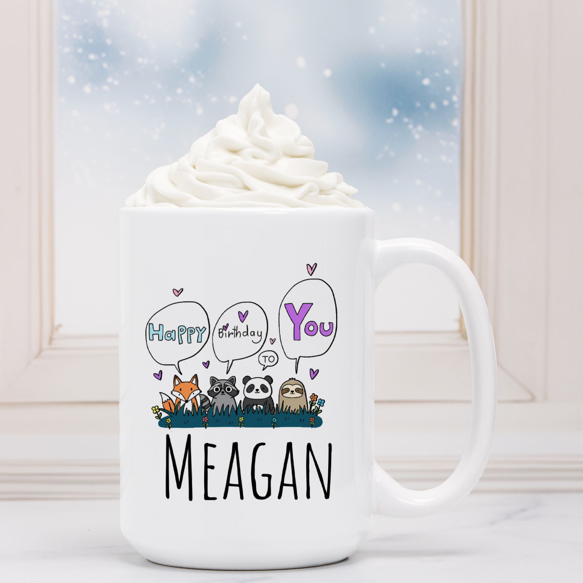 White mug with cartoon animals and 'Happy Birthday to You Meagan' text, filled with hot chocolate.