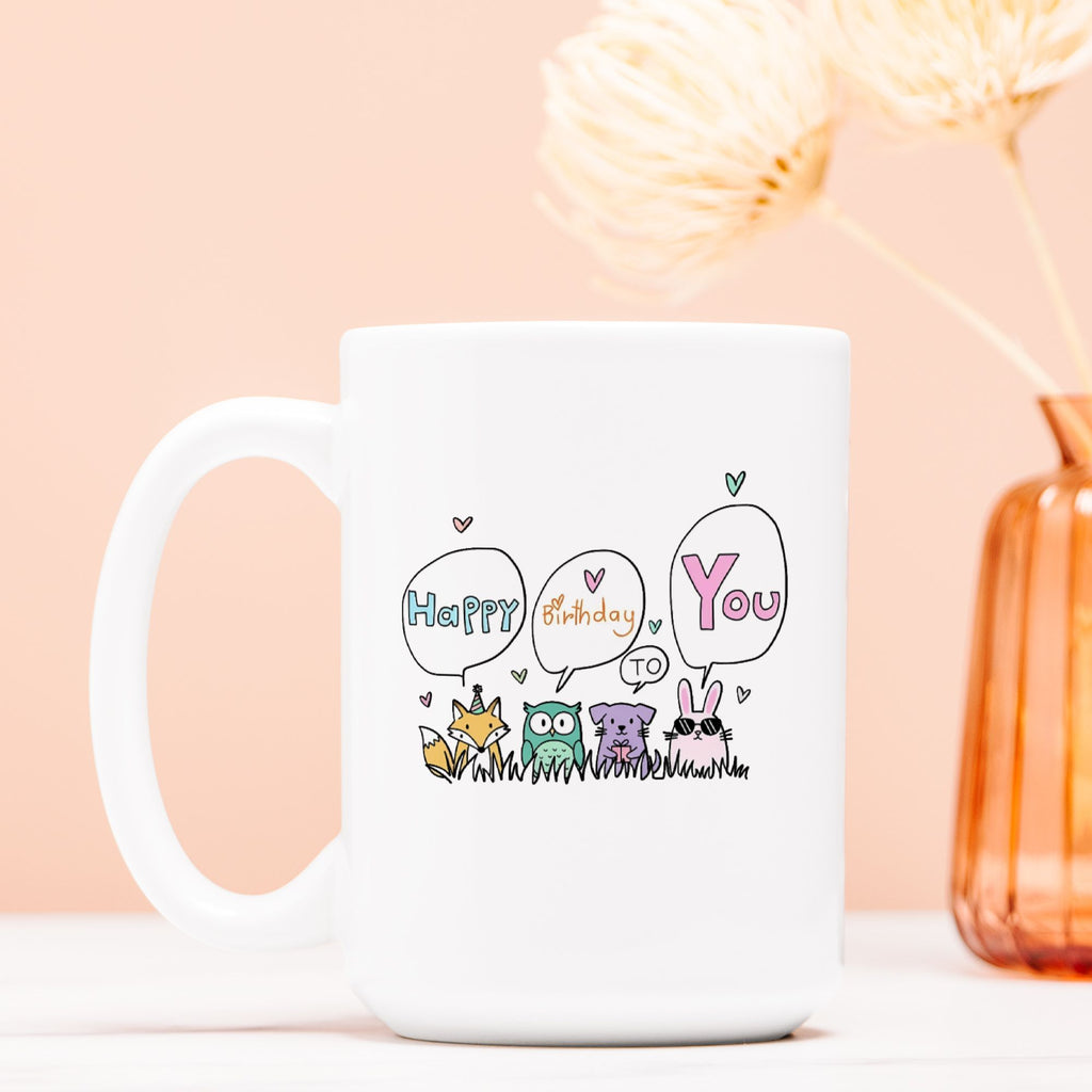 White mug with birthday design featuring cartoon animals and text on a light pink background.
