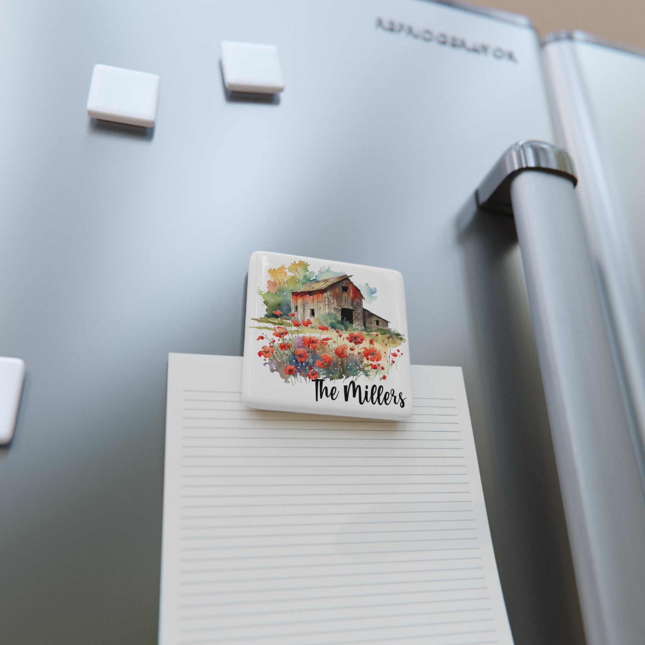 Fridge magnet with a house and flowers design on a refrigerator next to a notepad.