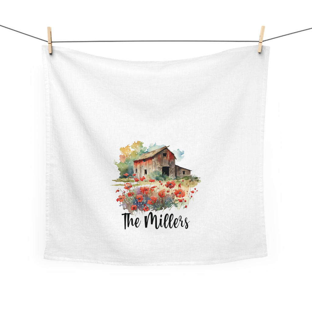 White tea towel with a barn and flowers design and 'The Millers' text, hanging on a line.