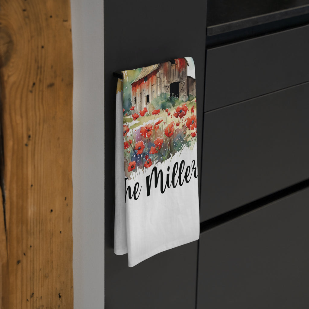 Tea towel with a barn and poppies design hanging on a black surface.