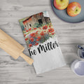 Tea towel with floral barn design and 'The Miller' text on a wooden surface with apples and a rolling pin.
