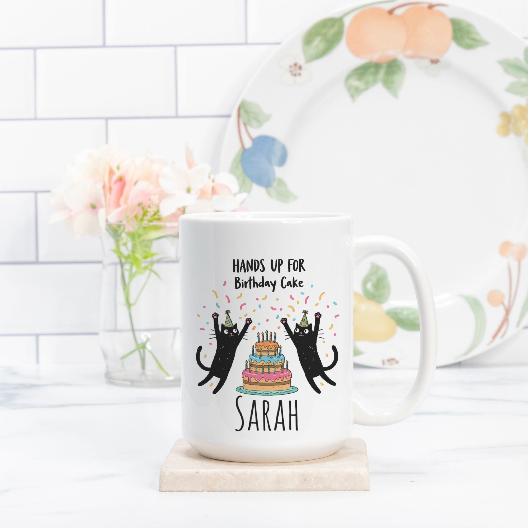 White mug with black cat design and text, placed on a white surface with a decorative plate in the background.