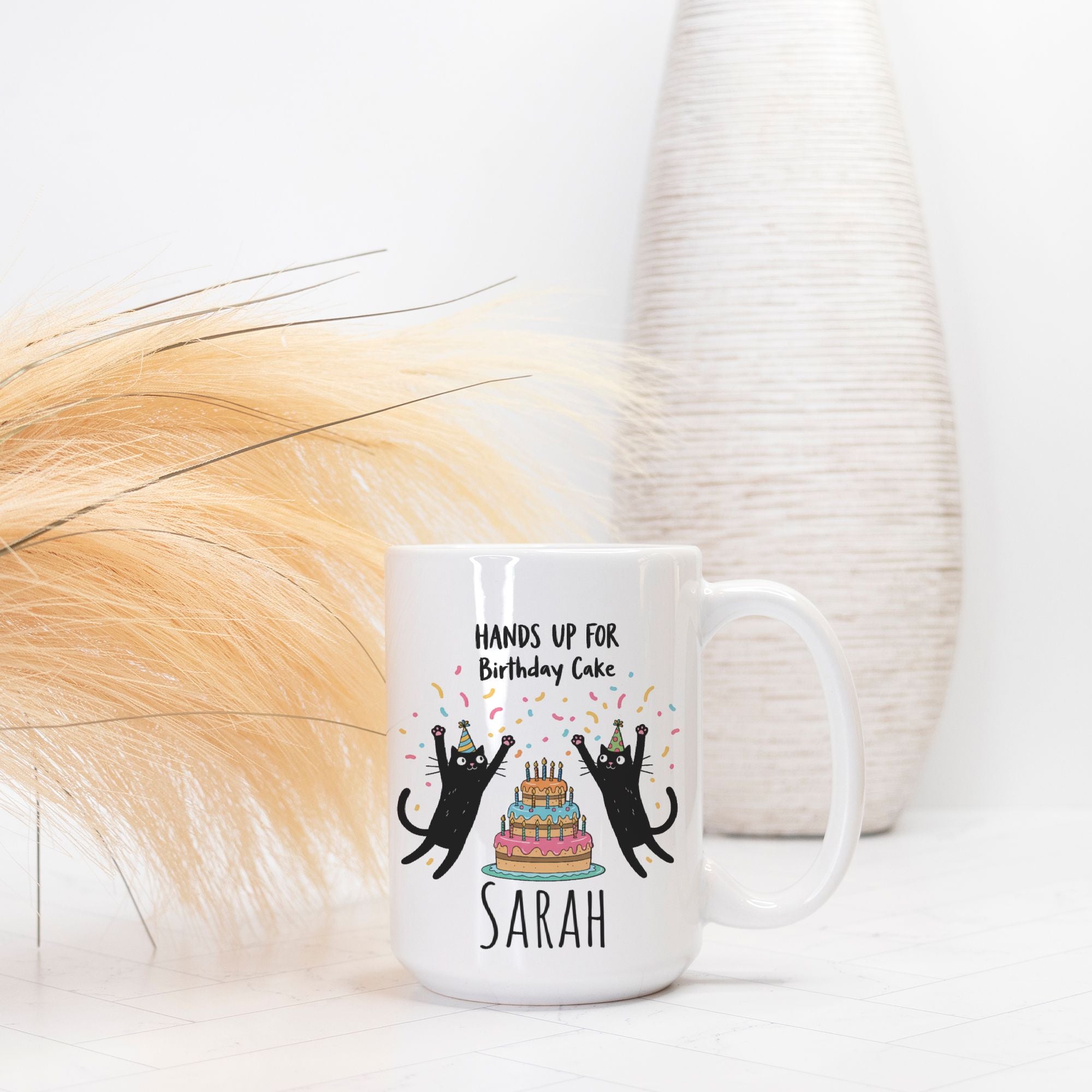 White mug with black cat design and text 'Hands up for Birthday Cake Sarah' on a white background