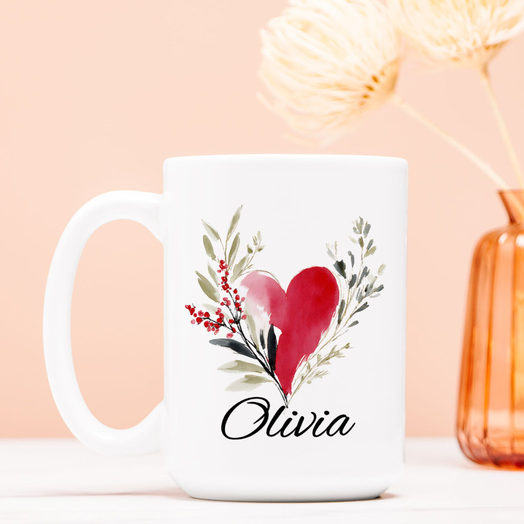 White mug with a red heart and green leaves design, featuring the name 'Olivia', on a light pink background.