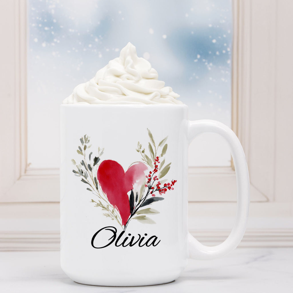 White mug with a red heart and green leaves design, filled with hot chocolate and whipped cream.