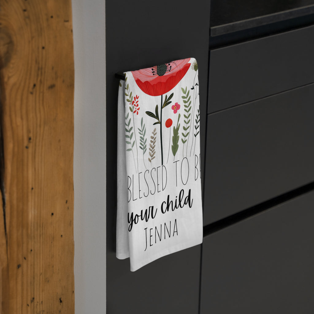 Decorative tea towel with floral design and personalized text hanging on a black cabinet.