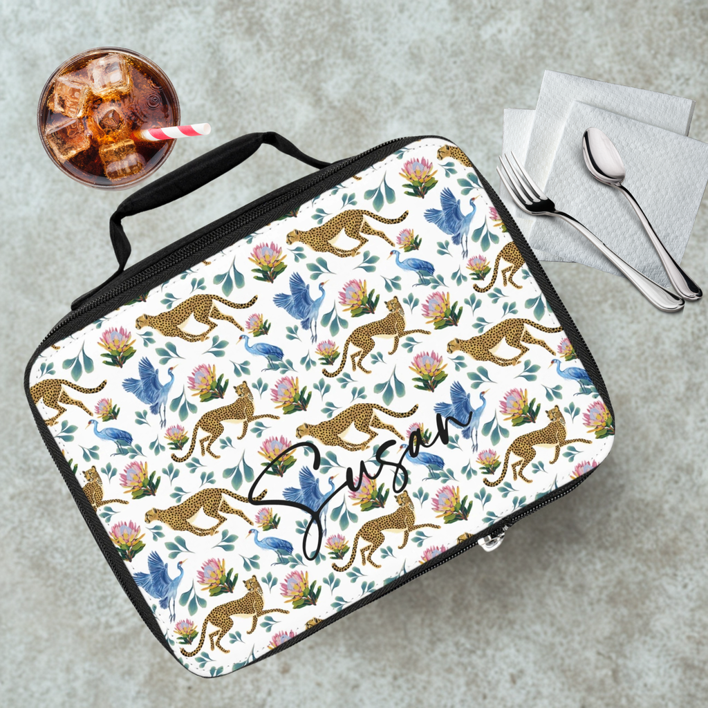 Lunch bag with animal pattern and 'Susan' text on a gray table with a drink and utensils.