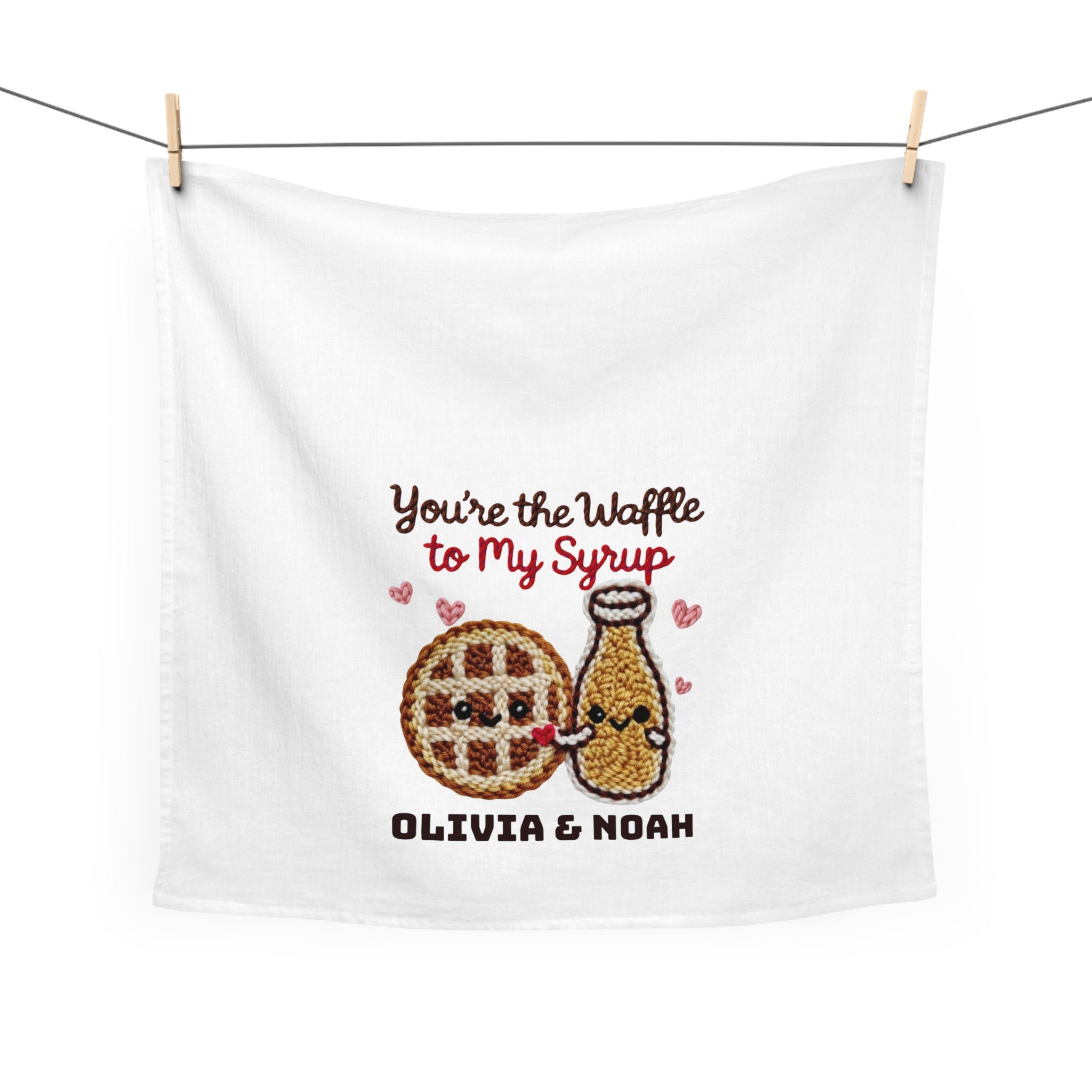 White towel with embroidered style design of a waffle and syrup bottle, text 'You're the Waffle to my Syrup Olivia & Noah', hanging on a line.