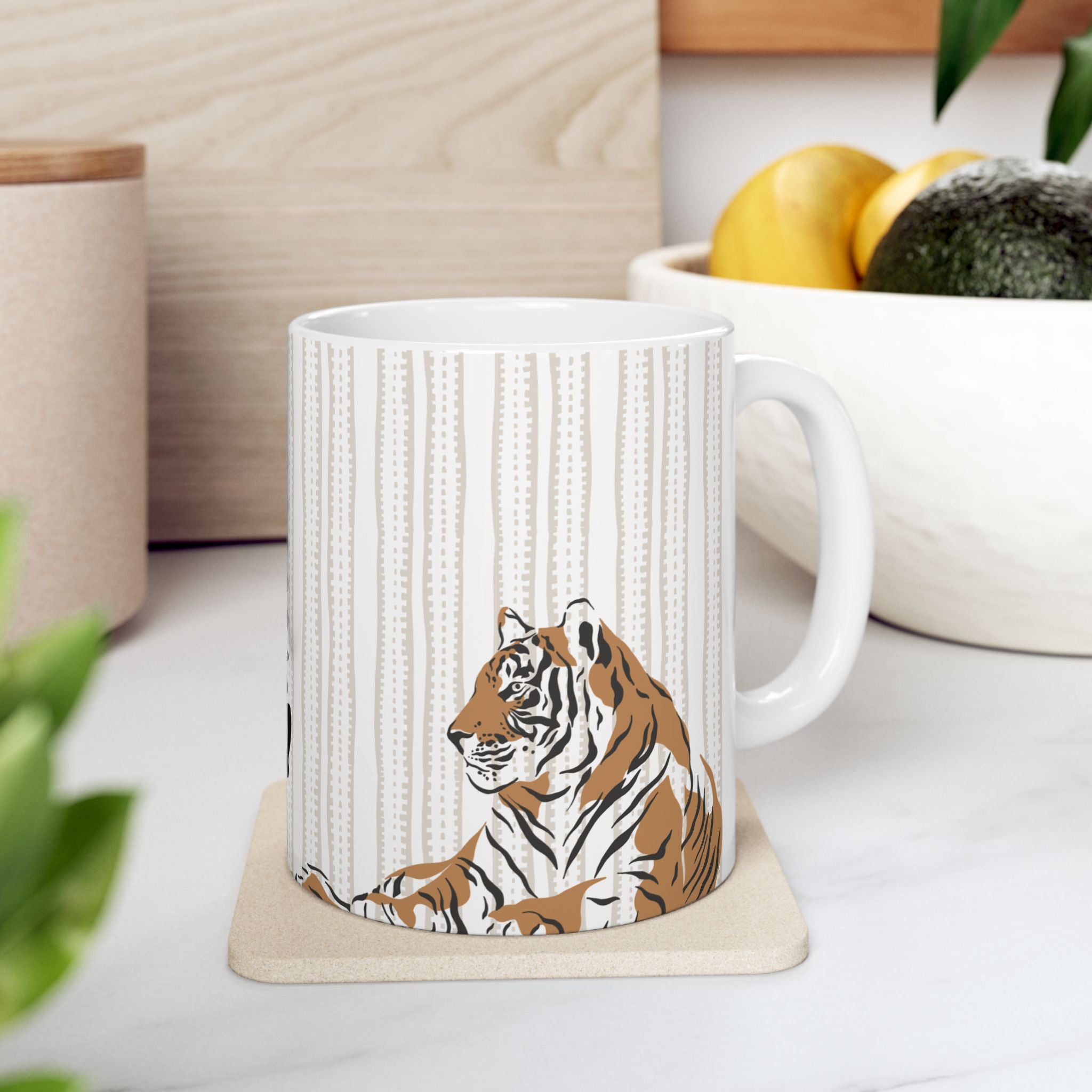 White 11oz mug with tiger design on a coaster, placed on a surface with a plant and container in the background.