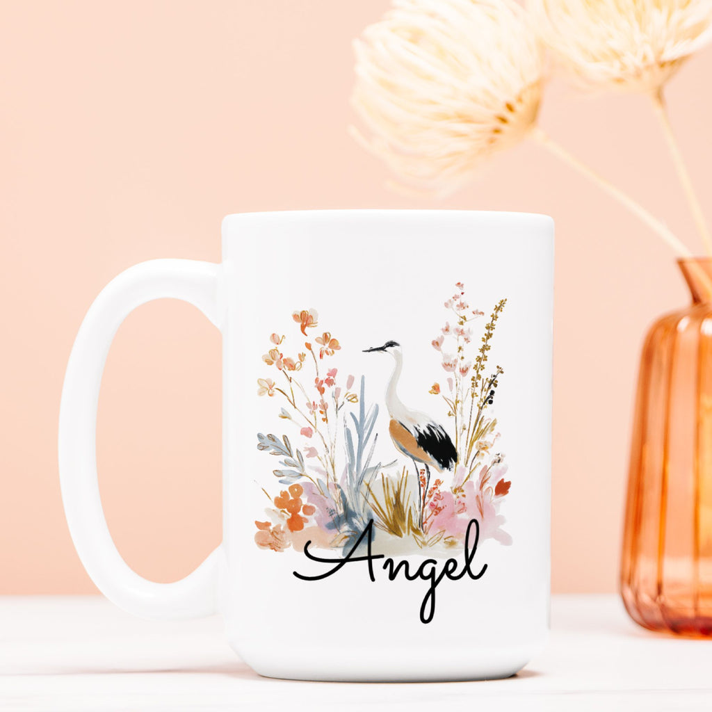 White mug with floral design and 'Angel' text on a light pink background