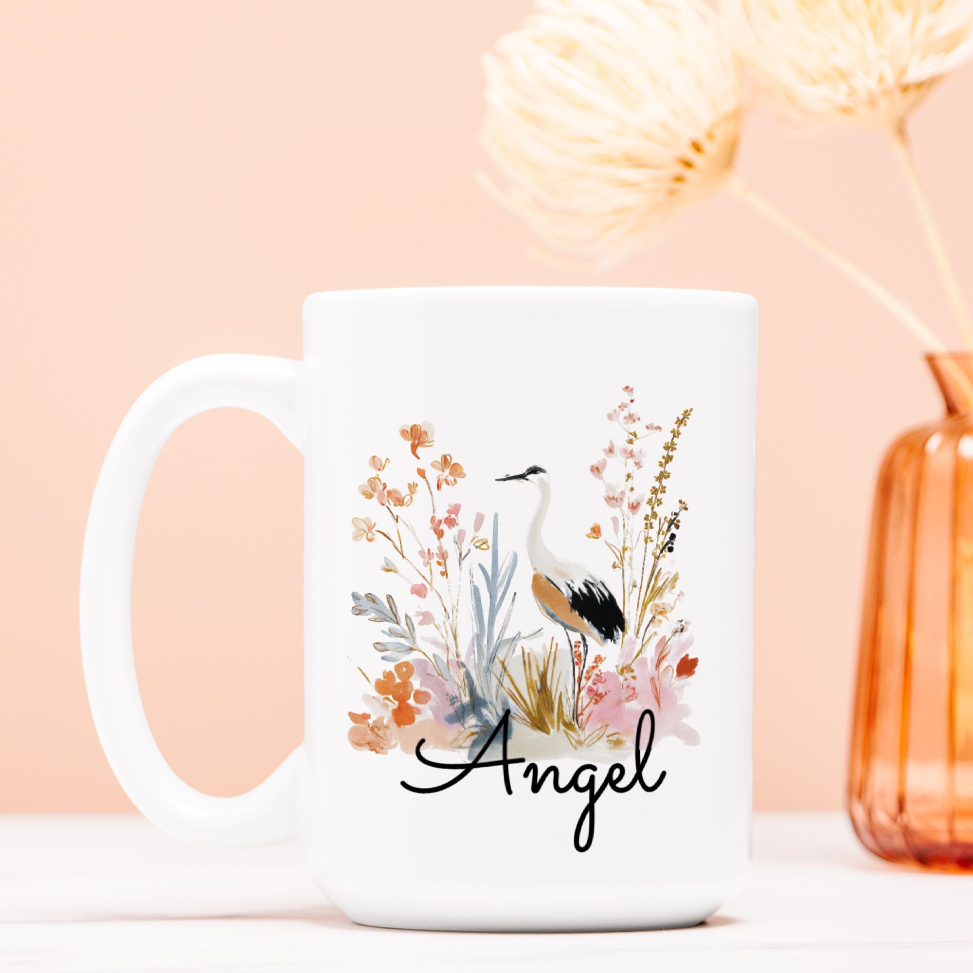 White mug with floral design and 'Angel' text on a light pink background