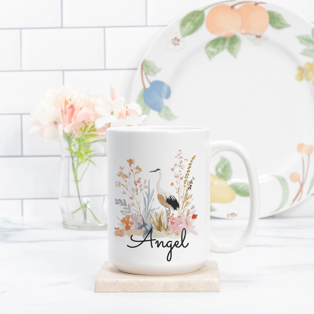 Mug with floral design and 'Angel' text on a white surface with a blurred background