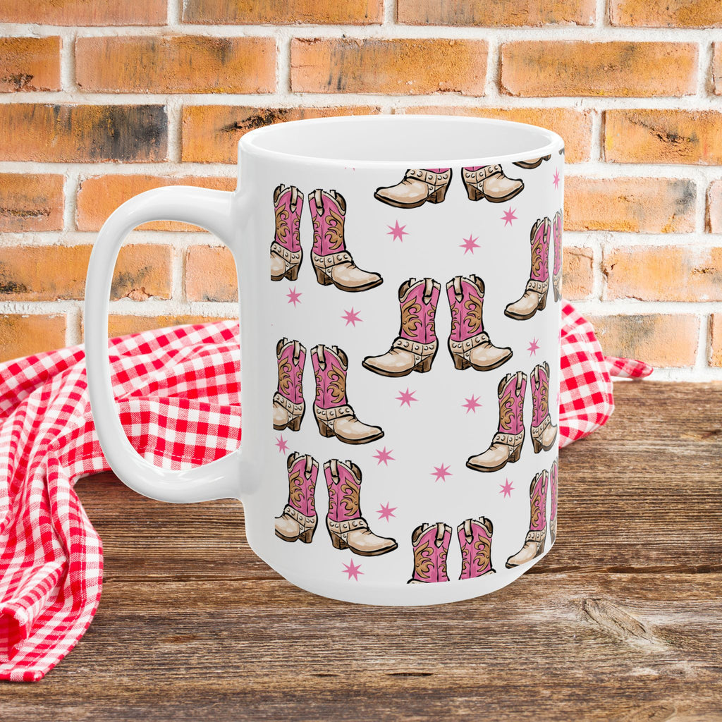 White mug with pink cowboy boot pattern on a wooden surface with a red checkered cloth and brick wall background.